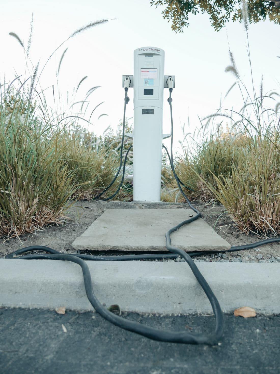 An electric vehicle charging station with its cable coiled on the ground.